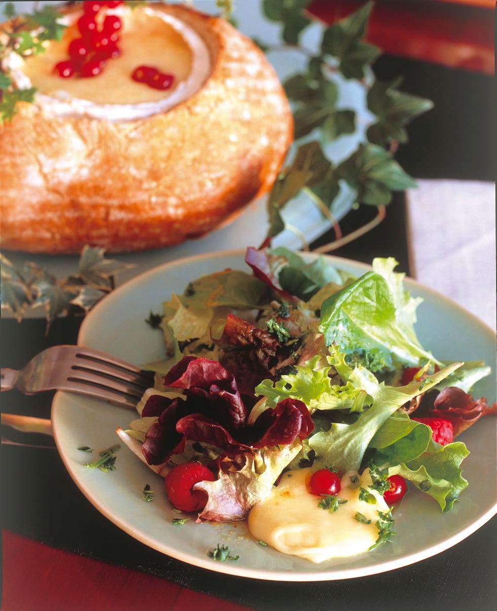 a plate of fresh salad with a side of creamy sauce and a large round bread bowl filled with a lightcolored dip topped with red berries