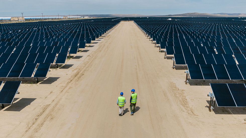 two workers walk in between solar cells on a desert road in california