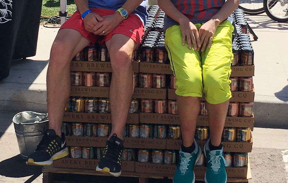 the legs of two runners sitting on many cases of beer.