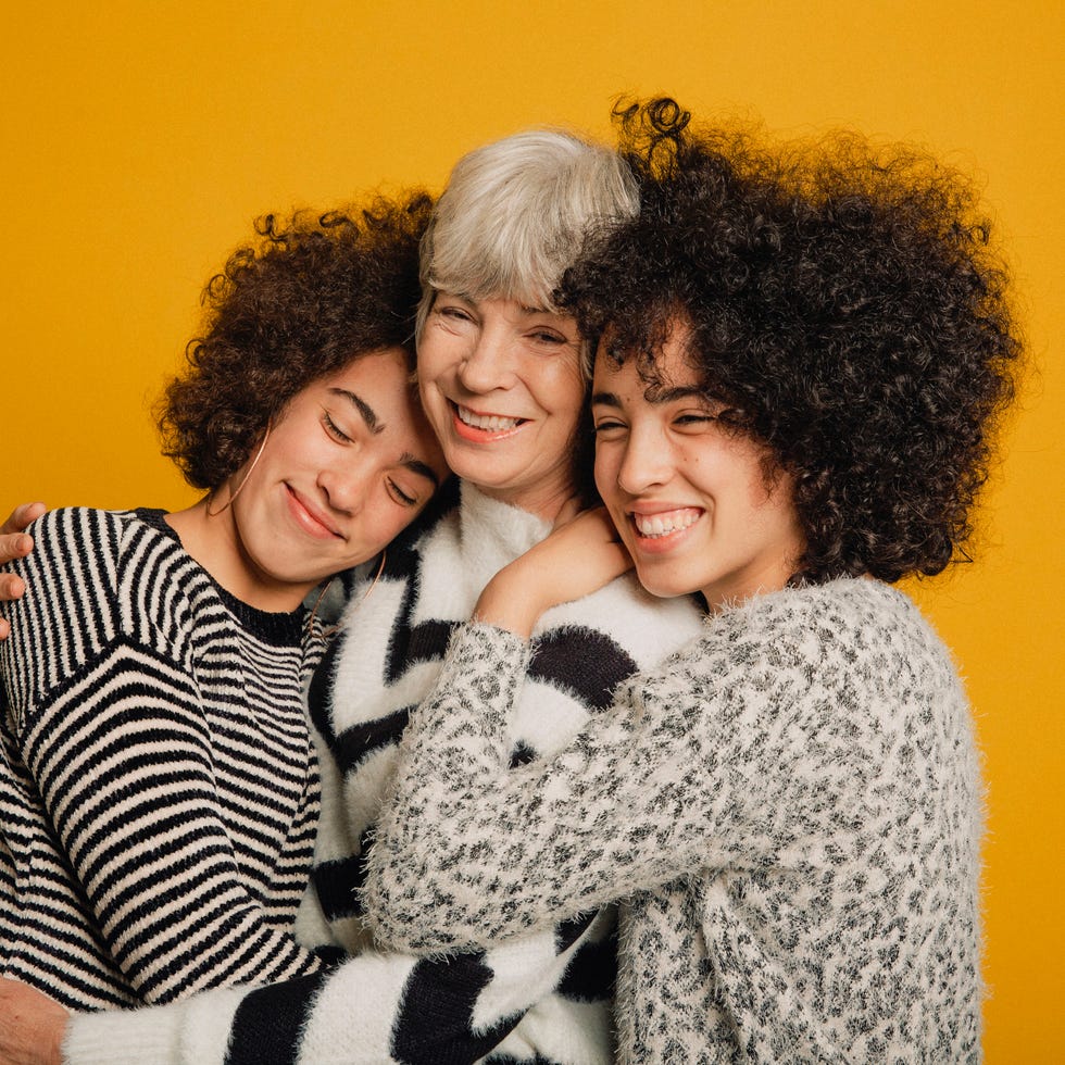 mid length portrait of two teenage female twins and their mature mother embracing in front of a yellow background
