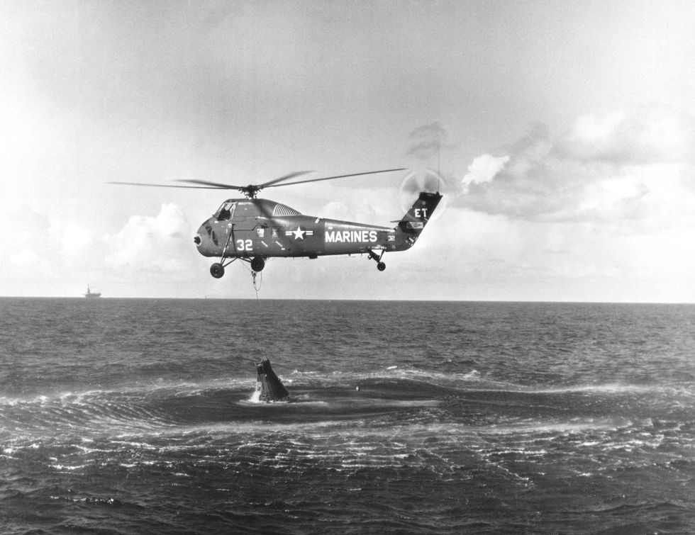 Een helikopter van deUS Navy probeert de gehavende Liberty Bell 7 uit het water te hijsen nadat het luik er onverwachts afvloog toen de capsule in zee neerkwam Iets rechts naast het midden is het hoofd van Gus Grissom te zien die zijn best moet doen om te blijven drijven omdat hij geen tijd had zijn pak goed te sluiten