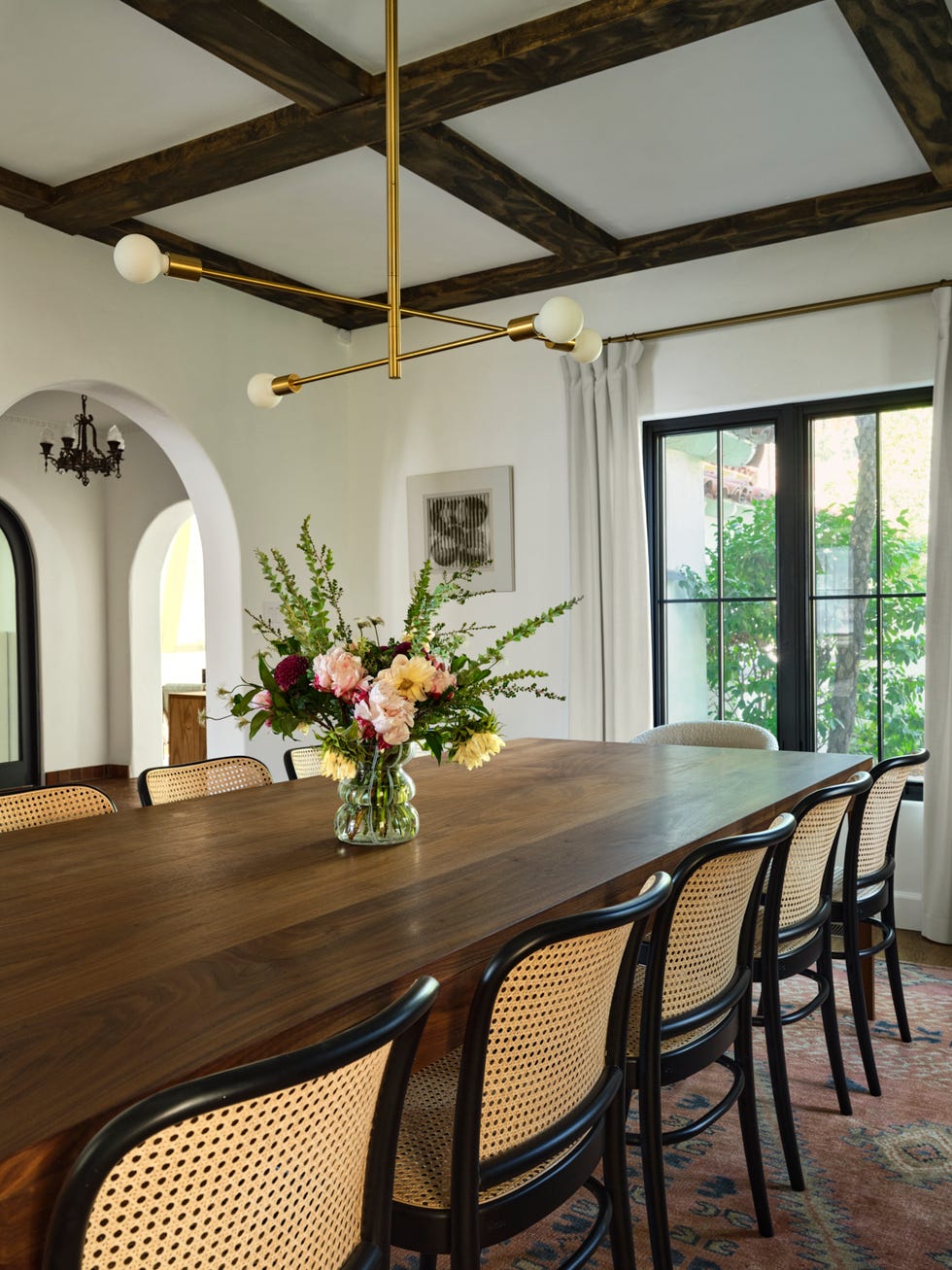 a spacious dining area with a long wooden table at its center, surrounded by several chairs with woven backs