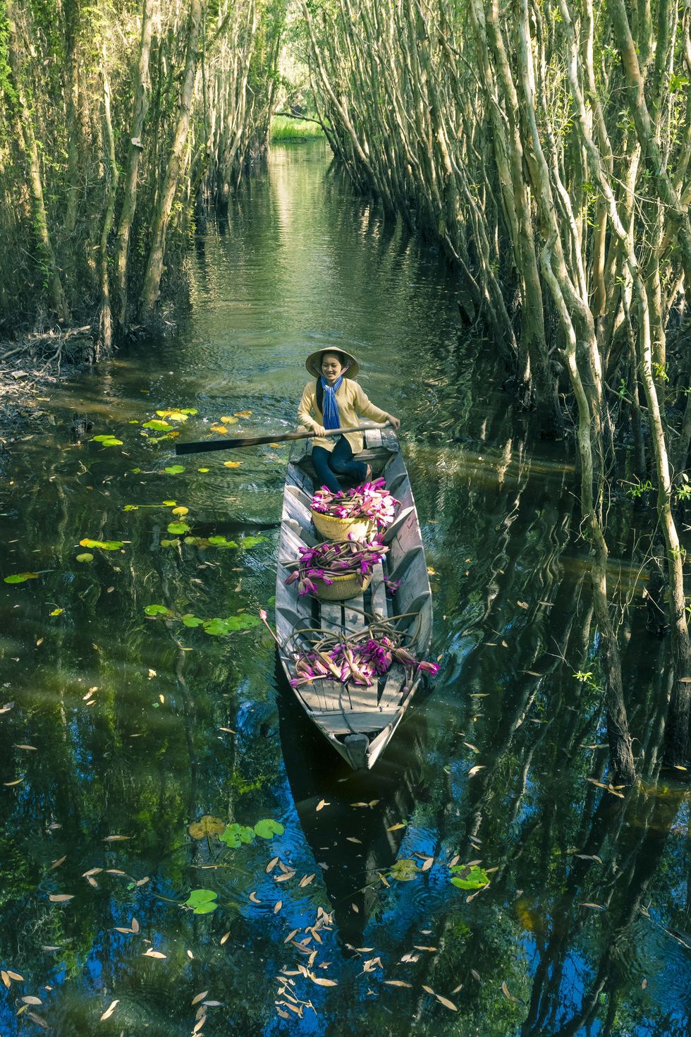 Young Vietnamese woman rowing boat loaded flowers