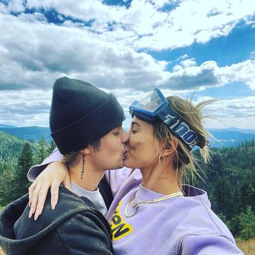 justin and hailey bieber share a kiss on a mountain, hailey wearing lilac and smiling