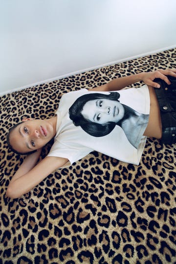 a model on a leopard print rug wears a t shirt from wales bonner's spring summer 2025 collection printed with a woman's face