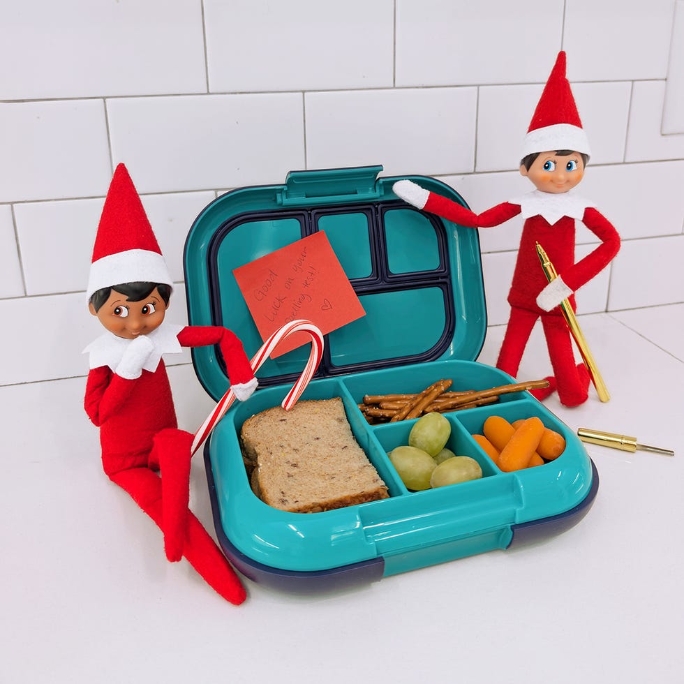 two elves pack a lunch one adds a note that says "good luck on your spelling test" while the other slips a candy cane into the lunchbox