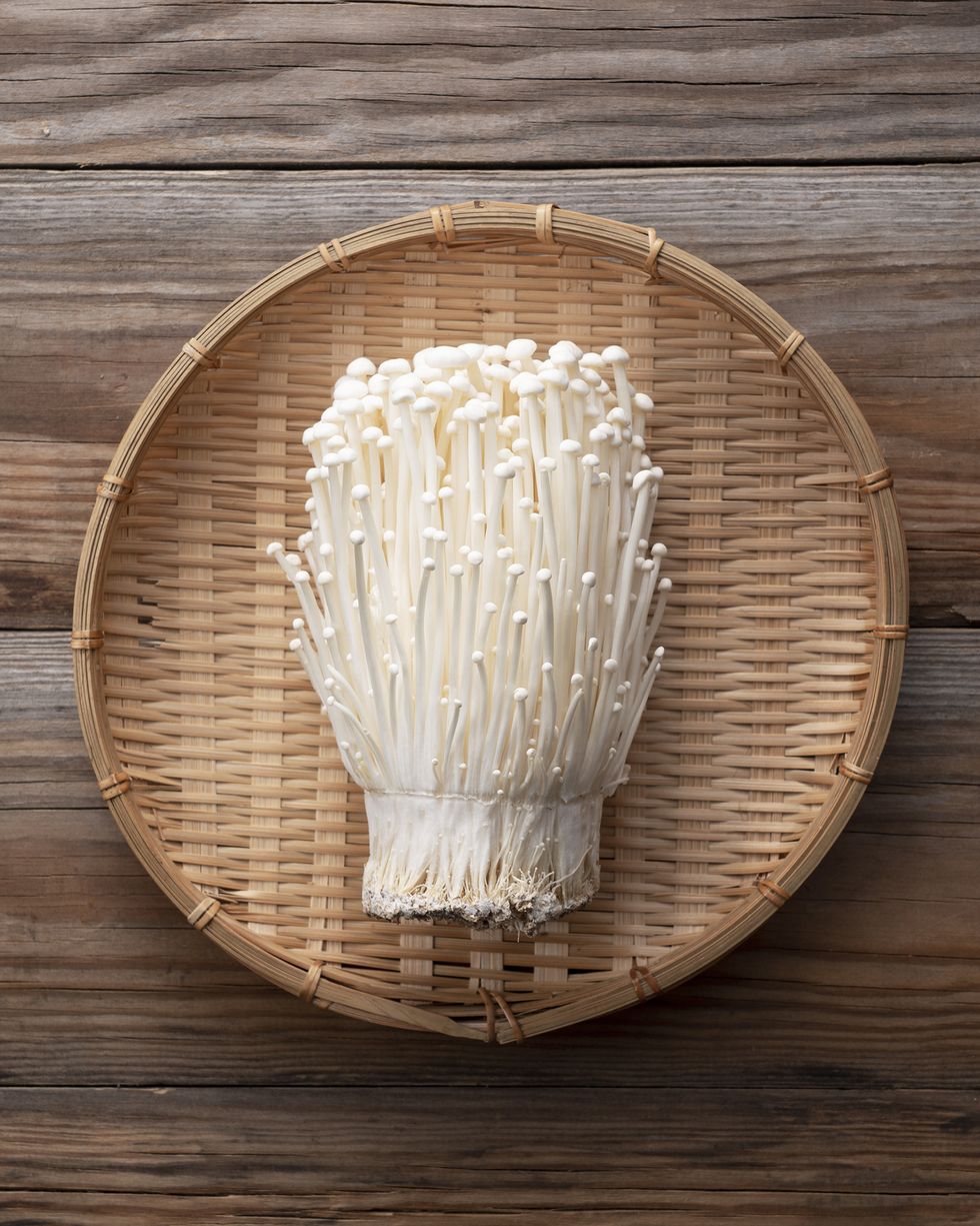 enoki mushrooms in a bamboo colander placed against a wooden background viewed from above