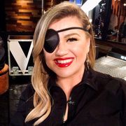 kelly clarkson sits with a black eye patch on her face in the background, 'the voice's leon bridges sits and smiles at the camera
