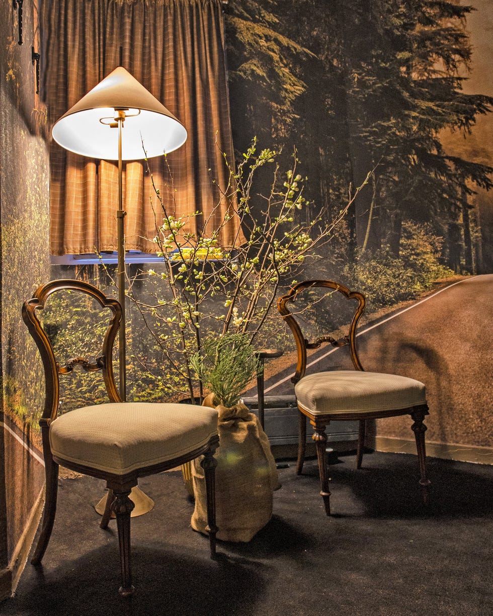 Cozy interior corner with two wooden chairs, a lamp, and decorative greenery.