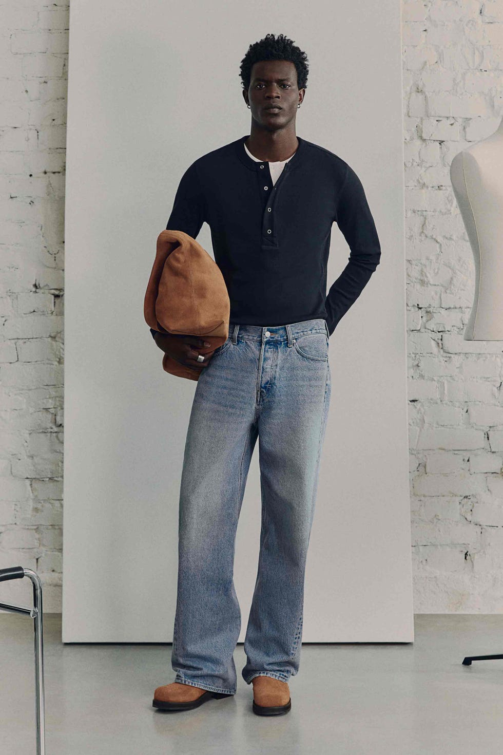 model wearing casual clothing with a hat in hand in a studio setting