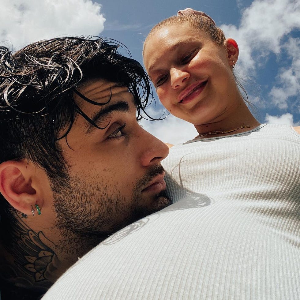 pregnant and smiling gigi hadid in a white tank top with zayn malik resting his head on her stomach, gazing up at her