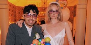 sophie turner and joe jonas posing stoically in matching sunglasses in front of a giant cake with "jonas" blue candles on top of it
