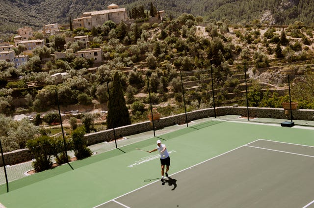 Tennis player practicing on a court with a scenic background.