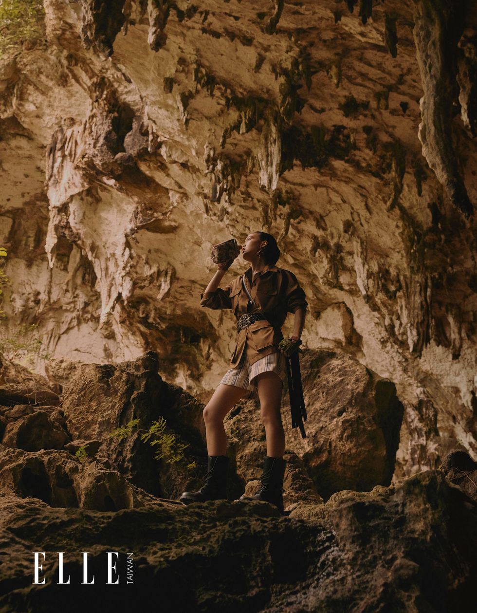 一個女人穿著獵裝夾克、百慕達短褲，站在鐘乳石洞中