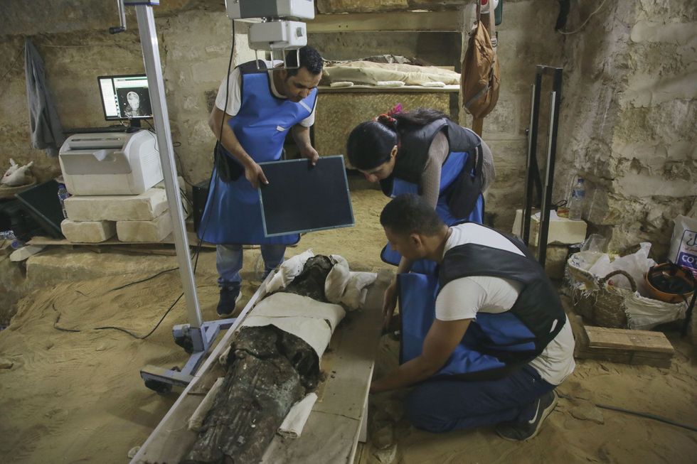 Paleoradioloog Sahar Saleem tussen de twee mannelijke technici gebruikt een mobiel rntgenapparaat om de geheimen te ontdekken die verstopt zitten onder de doeken van de gemummificeerde priester Ayput De naam is mannelijk maar de afmeting en vorm van het bekken van de mummie evenals de ronde vorm van de schedel doen Saleem vermoeden dat deze priester eigenlijk een priesteres was