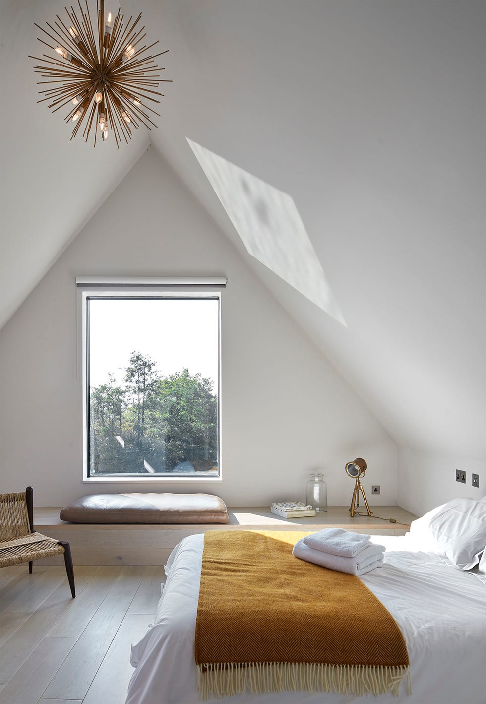 a bedroom with white walls, wooden floors, white bed linen, and a wooden bench at the end wall underneath a window