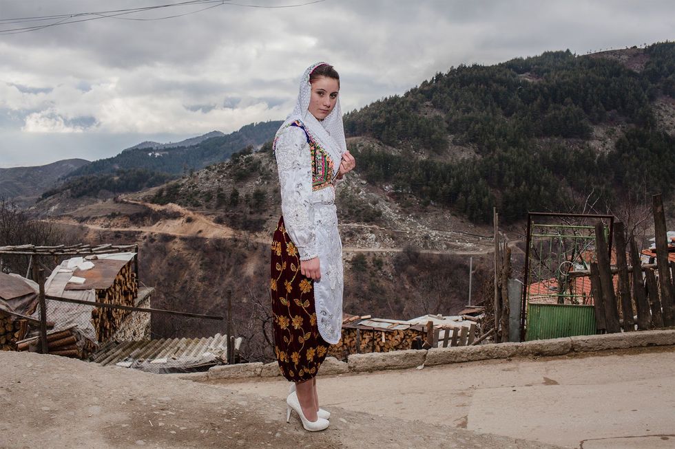 Met traditionele kleding loopt een jonge vrouw in Ribnovo naar de huwelijksceremonie van Letve Osmanova en Refat Rvdikov