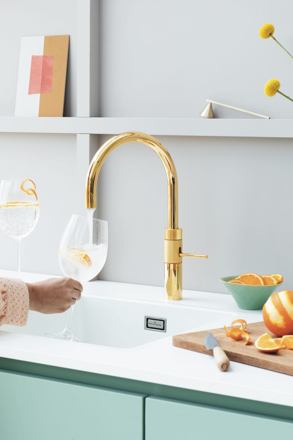 kitchen scene featuring a gold faucet and a person pouring water into a glass
