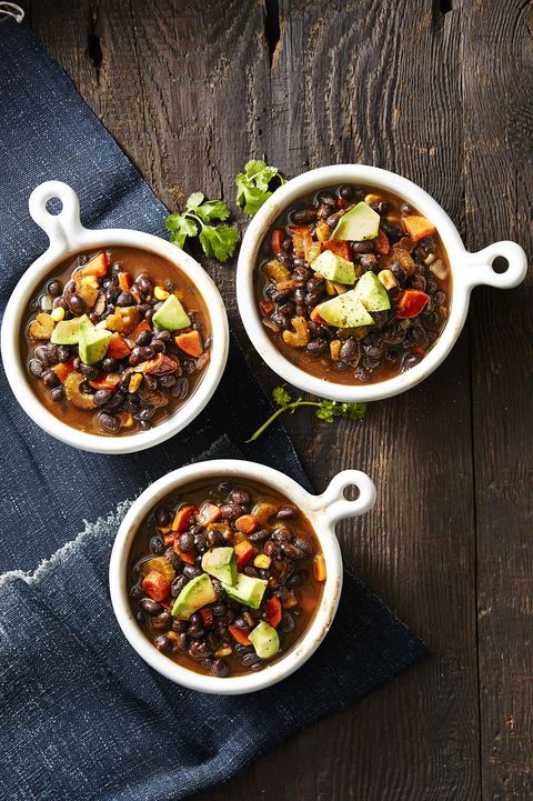 white bowls of black bean soup with slices of avocado
