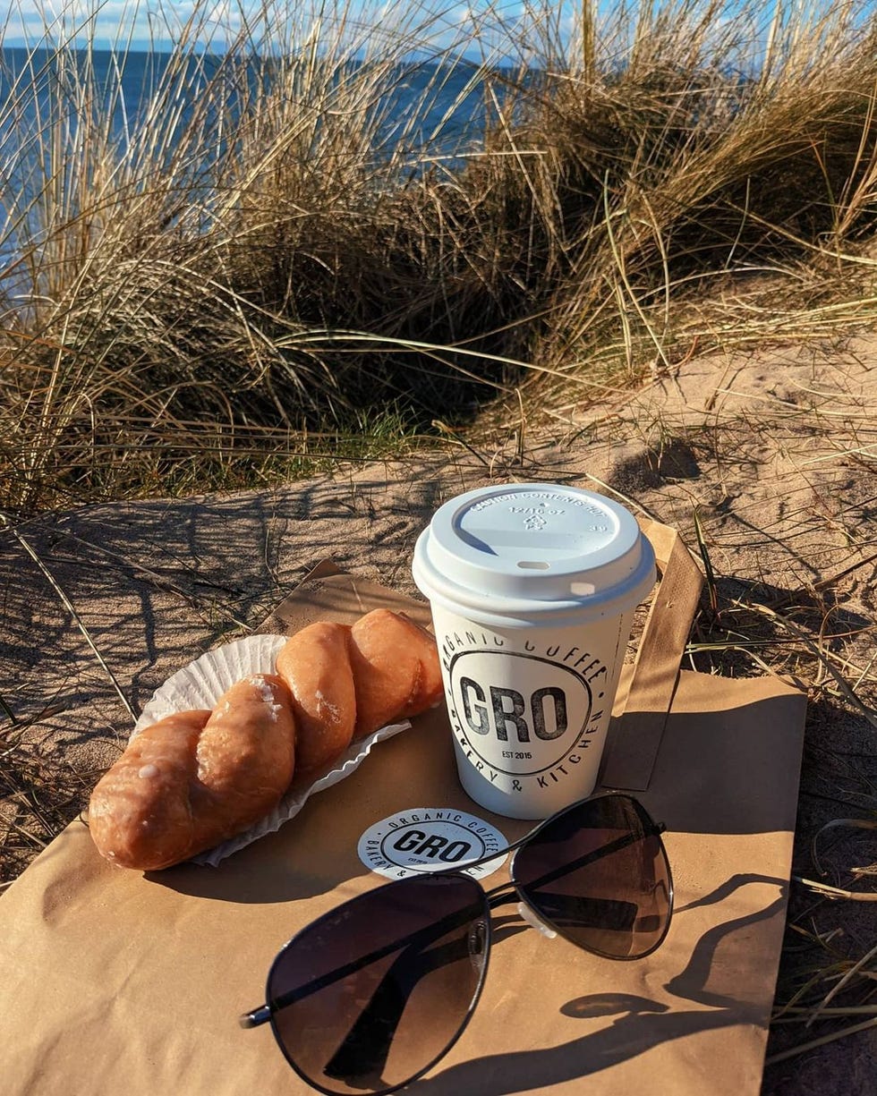 a takeaway coffee cup and a pastry on sand by the sea
