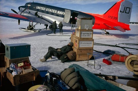 Op Antarctica rust een man uit tegen voorraadkisten terwijl de rest van de bemanning zich voorbereidt op een vlucht