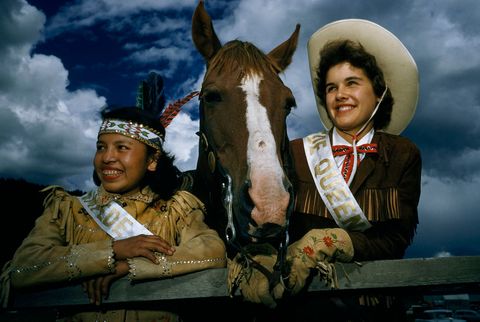 Dit portret van twee rodeokoninginnen en een paard die kijken naar de festiviteiten in Williams Lake British Columbia verscheen in de editie van augustus 1958 Het verhaal vierde het 100jarig bestaan van de Canadese provincie