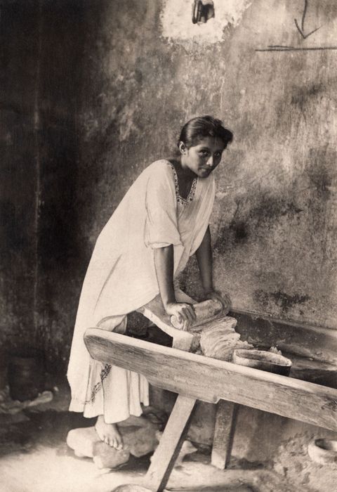 In Mexico poseert een vrouw voor de foto terwijl zij met een maalsteen of metate graan maalt 1914