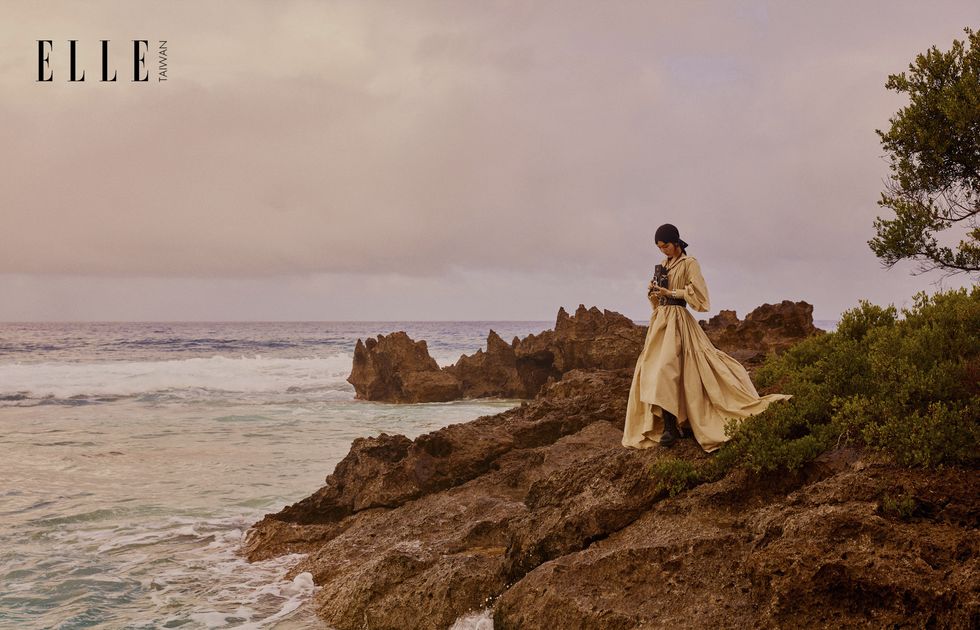 一個女人穿著襯衫連衣裙站在礁岩岸上