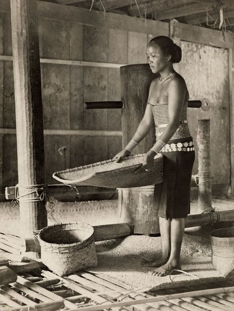 In Sarawak op Borneo zeeft een Dajakvrouw rijst nadat die is gedorst in een molen 1919