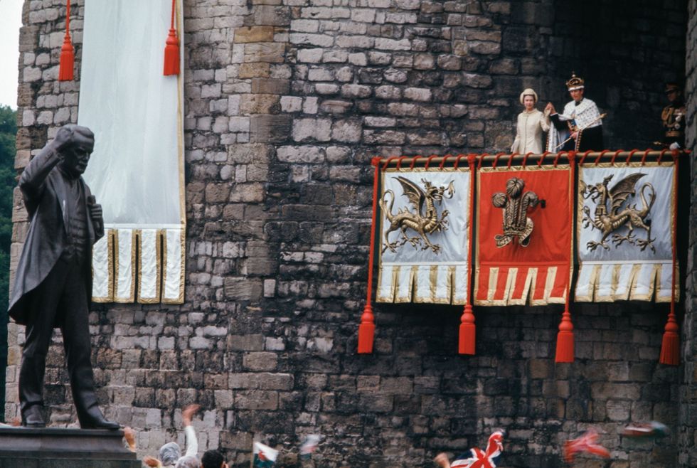Na de plechtige ceremonie waarbij kroonprins Charles als Prince of Wales is genstalleerd in 1969 wuiven Elizabeth II en prins Charles naar de menigte Hoewel Charles de titel ontving vond de ceremonie plaats tegen de achtergrond van een groeiend Welsh nationalisme