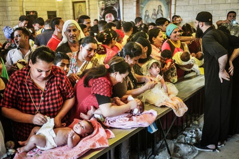 Vrouwen leggen hun babys op een rij zodat ze kunnen worden gedoopt tijdens het moulidfestival van Gabal alTayr Er zijn zoveel babys dat ze in groepen als op een lopende band worden gedoopt En priester neemt de eed af een andere dompelt ze in het water en een derde zegent ze met olie