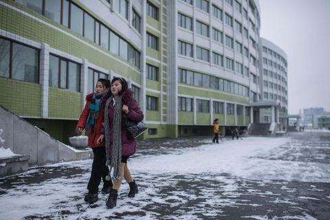 Vrouwen lopen langs woonverblijven voor arbeiders van de zijdefabriek Kim Jong Suk in 2013 opende de fabriek deze verblijven en tevens een dagopvang waar elke dag tweehonderd kinderen worden verzorgd terwijl hun moeders werken