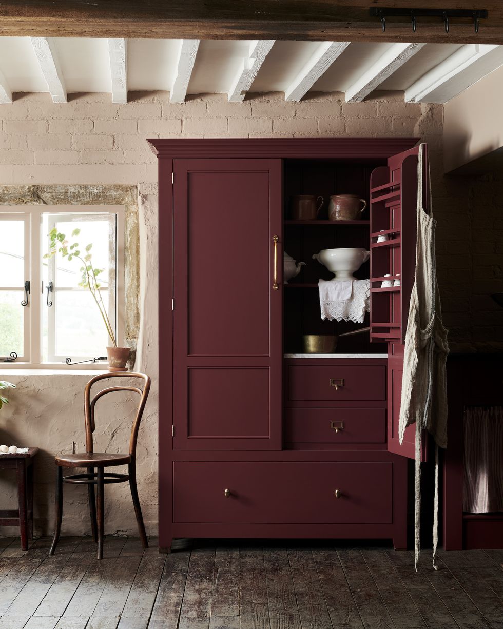a dark red freestanding pantry in a pale pink kitchen