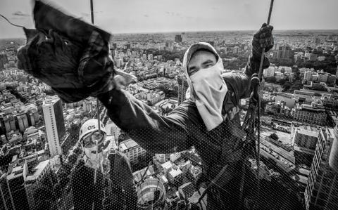 Deze ramenwassers werken 50 of 60 verdiepingen hoog in Ho Chi Minh City in Vietnam Your Shotfotograaf Huynh Dung noemt hen dapper en wijst erop dat ze niet alleen op kleine schommels hoog in de lucht staan maar dat ze hun werk ook nog eens onder de hitte van de zon doen
