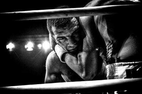 Een man staart in de camera terwijl hij tijdens een bokswedstrijd in de houdgreep wordt gehouden door zijn tegenstander