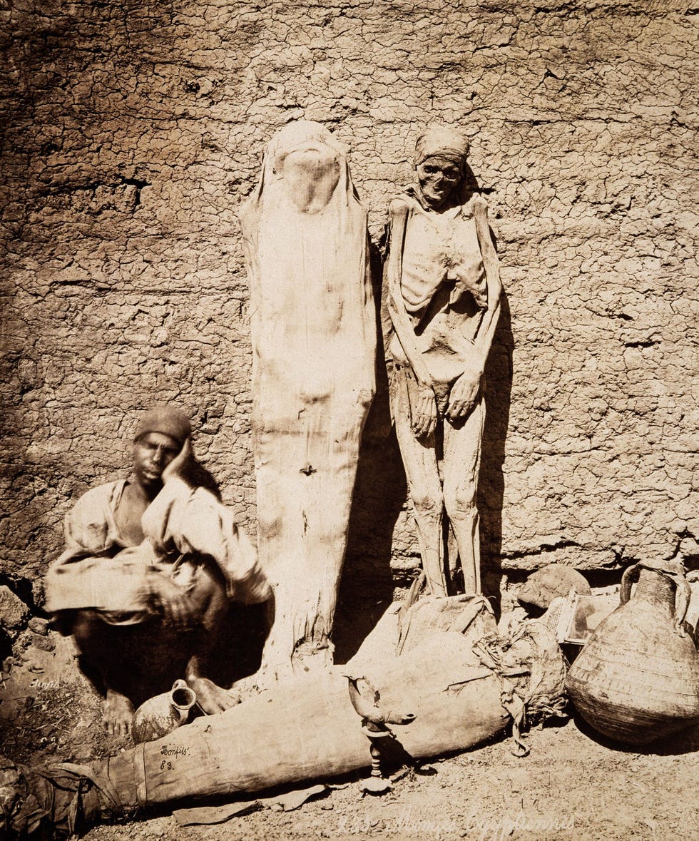 MUMMIEMARKT  De mummierage leidde tot een macabere handel in souvenirs Op deze foto uit circa 1877 zit een Egyptische handelaar in mummies naast zijn koopwaar