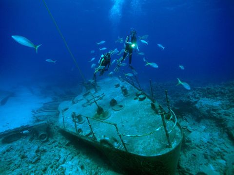 Duikers en vissen zweven boven de resten van een schip dat op een van de vele koraalriffen rond de Kaaimaneilanden in de Carabische Zee is gelopen