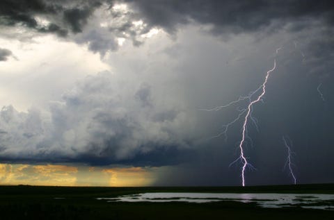 Een monsterwolk produceert bliksemschichten terwijl het op de achtergrond begint te regenen