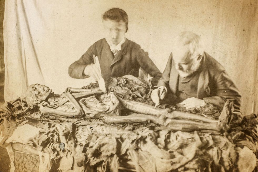 ZORGVULDIGE OMGANG  Op deze foto uit de negentiende eeuw zijn twee onbekende mannen bezig met de voorzichtige autopsie van een mummie wat laat zien hoe de academische houding jegens Egyptische oudheden veranderde Het afwikkelen van een mummie werd steeds minder gezien als vermaak en steeds meer als serieus wetenschappelijk onderzoek