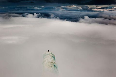 Bovenop de bergtoptoren van de Snaefellsjokull berg in IJsland staat klimmer Remi McMurtry boven de wolken Staand op de hogere rand rilde ik terwijl ik wachtte tot de wolken weg waren een 30 minuten pose voor 30 seconden helderheid De wolken zakten later naar beneden terwijl we omlaag wandelden in een middernachtzon