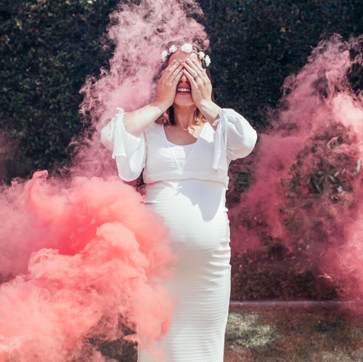 Happy pregnant woman covering her face with smoke grenade outdoors. Gender reveal party.