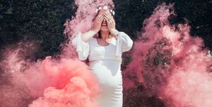 Happy pregnant woman covering her face with smoke grenade outdoors. Gender reveal party.
