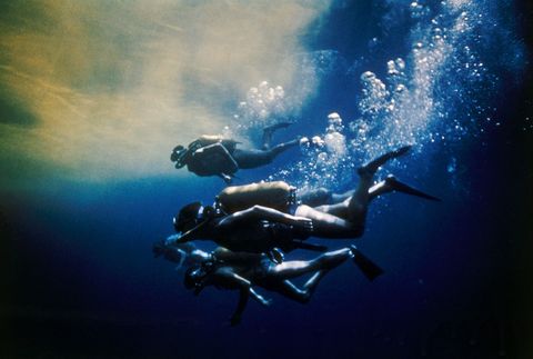Duikers zwemmen in de Indische Oceaan als onderdeel van een van Jacques Cousteaus expedities in de jaren 1950 Het water wordt gekleurd door een kleurstof die de duikers helpt hun weg terug te vinden naar de boot  de beroemde Calypso van Cousteau