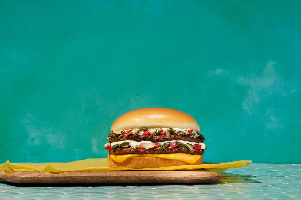 a burger with two beef patties cheese and a variety of toppings served on a wooden platter