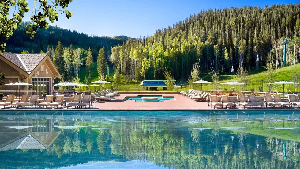 a pool with chairs and umbrellas by a house and trees