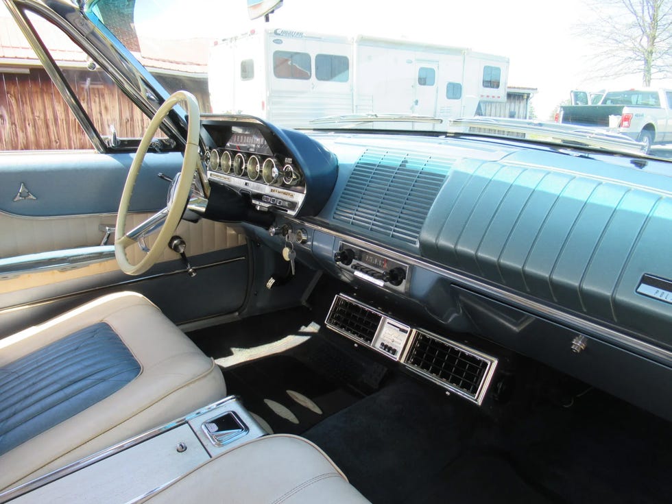 interior of a 1962 dodge polara 500, showing a two tone dashboard, steering wheel, and front seats with blue and white upholstery.
