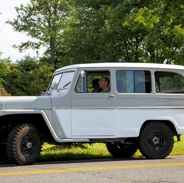 a white and grey 1962 willys jeep station wagon sits on the side of a road with trees in the background