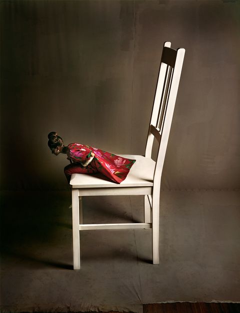 a model in a red dress and coat sits on a comically oversized white chair in this 1963 fashion photo
