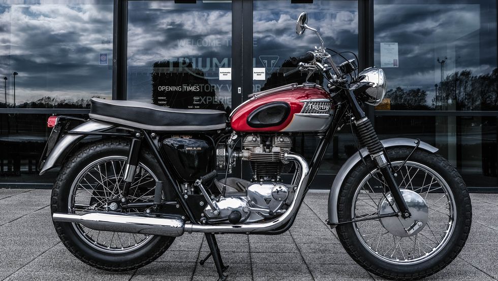 a 1964 triumph tr6 motorcycle in red is parked in front of a building