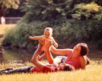 1970s couple lying in grass holding baby up above father (photo by photo media/classicstock/getty images)
